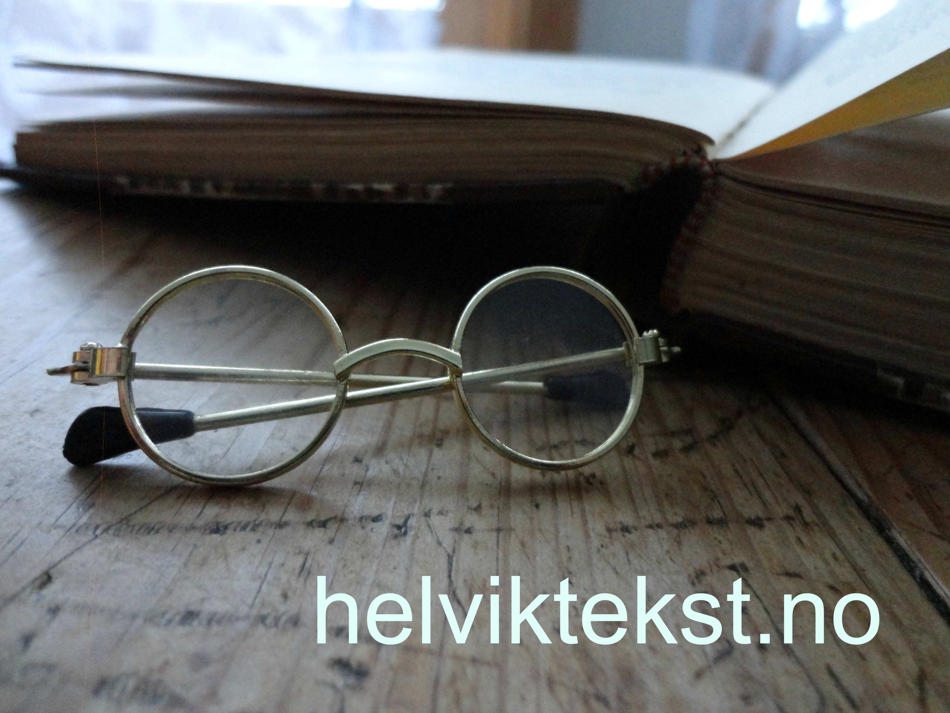 Bilete av nokre små briller i gamal stil framfor ei bok.